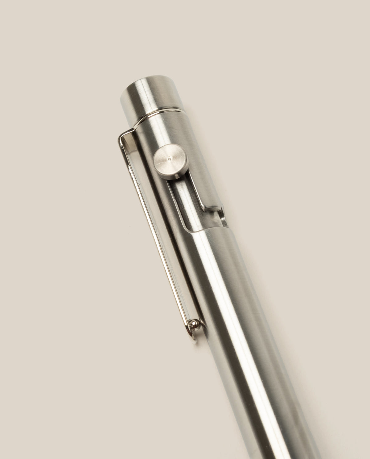 A close-up of the INVENTERY Bolt Action Pen (Stainless) with a clip, highlighting its sleek stainless steel design against a plain, light beige background.