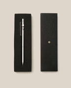 The INVENTERY Bolt Action Pen (Stainless) with a clip is displayed in an open black gift box next to its closed lid, which features a small gold emblem, all arranged on a light beige background.