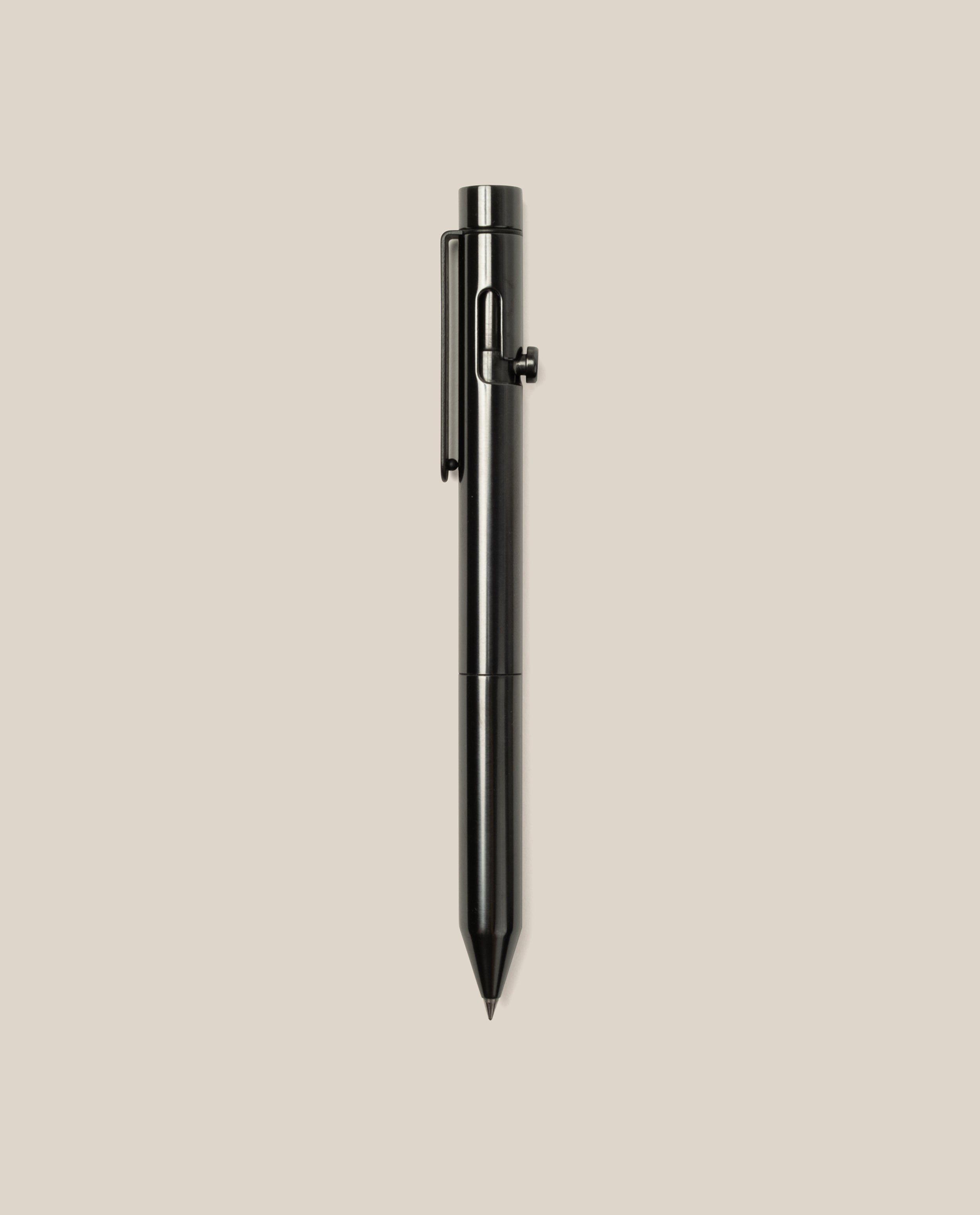 The INVENTERY Bolt Action Pen (Zirconium), featuring a sleek black metal design and a sturdy clip, stands upright against a plain light beige background.