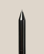 A close-up of the tip of the INVENTERY Bolt Action Pen (Zirconium)—a luxury black ballpoint pen—against a plain beige background.