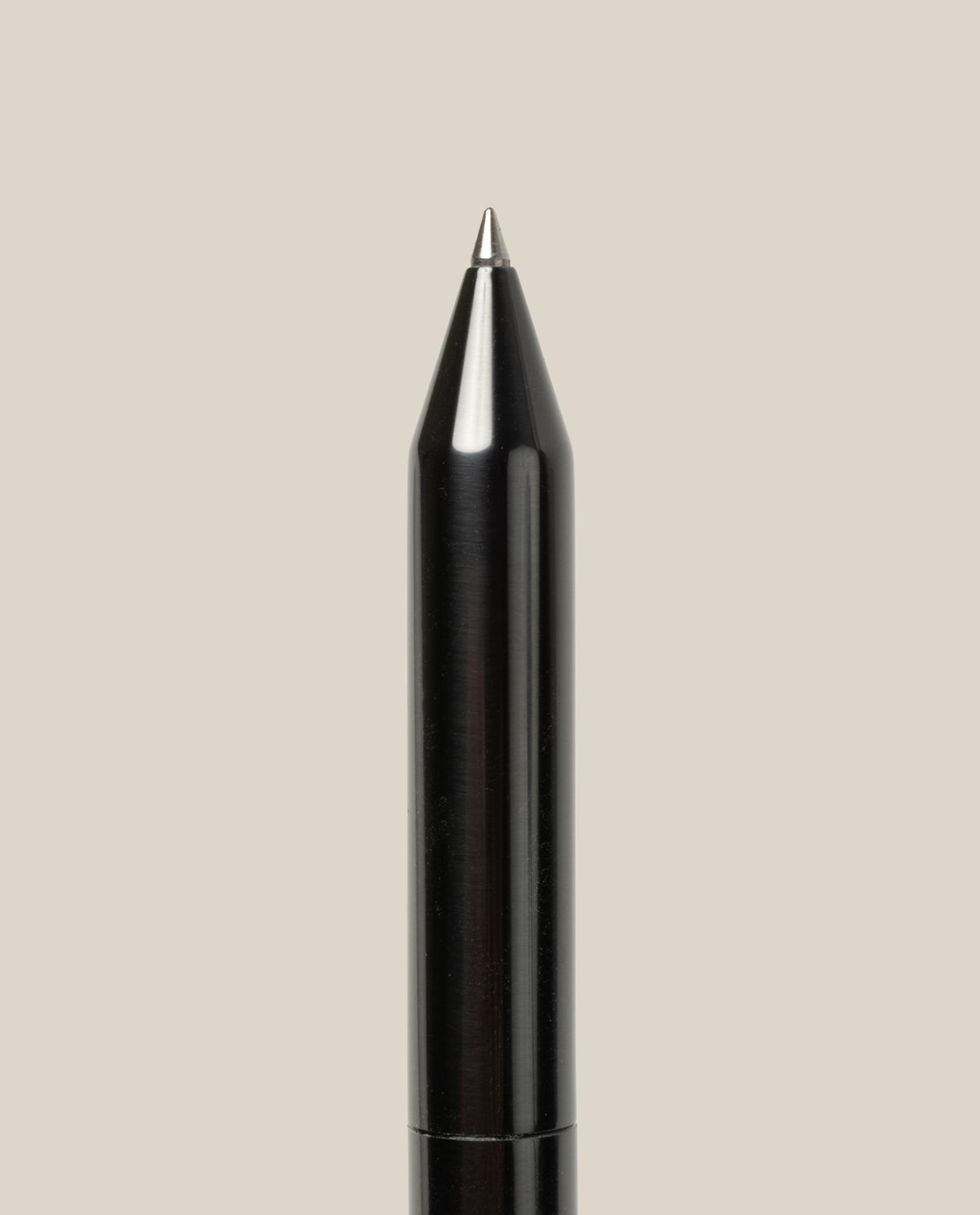 A close-up of the tip of the INVENTERY Bolt Action Pen (Zirconium)—a luxury black ballpoint pen—against a plain beige background.