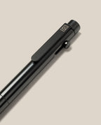 A close-up of the INVENTERY Bolt Action Pen (Zirconium), a sleek black writing instrument with a clip, set against a light beige background. Featuring a modern design and a small square logo near the top, this pen exemplifies the elegance of luxury craftsmanship.