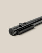 A close-up of the INVENTERY Bolt Action Pen (Zirconium) with its distinctive clip, resting diagonally on a light beige surface. Both the button and tip of this luxury writing instrument are prominently visible.