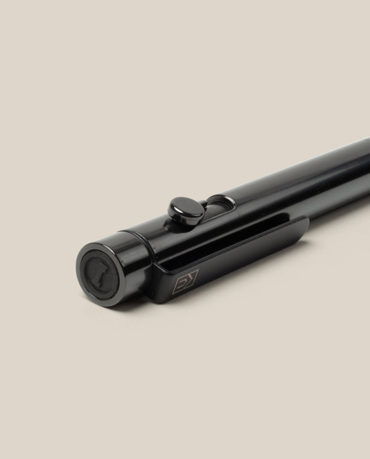 A close-up of the INVENTERY Bolt Action Pen (Zirconium) with its distinctive clip, resting diagonally on a light beige surface. Both the button and tip of this luxury writing instrument are prominently visible.