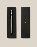 An INVENTERY Bolt Action Pen (Zirconium) rests in a sleek black gift box, with the box lid placed next to it on a beige background.