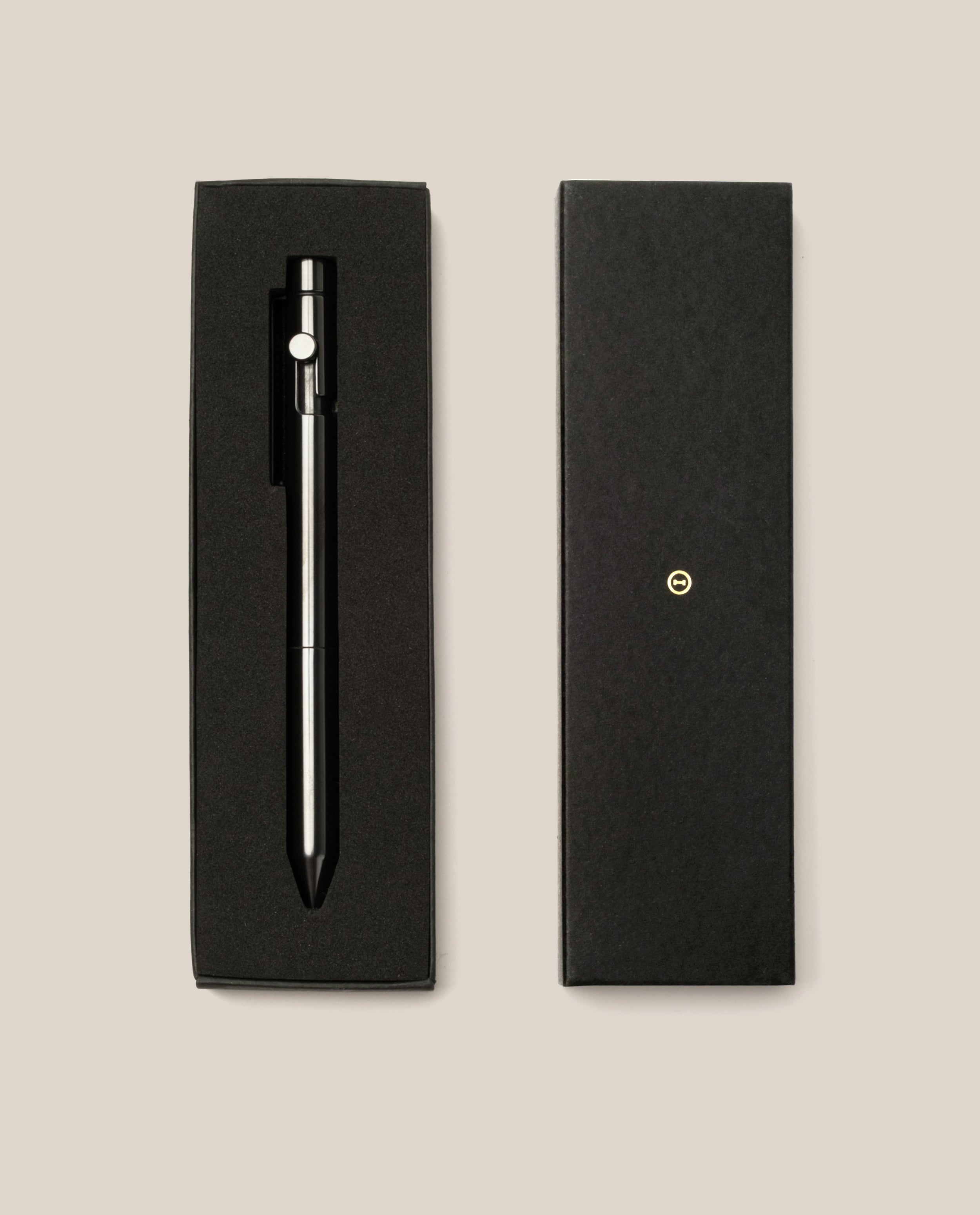 An INVENTERY Bolt Action Pen (Zirconium) rests in a sleek black gift box, with the box lid placed next to it on a beige background.