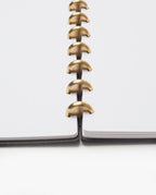 Close-up of the open Warehouse Item - Discbound Heirloom Journal (Black/Brass) with white dotted pages and brass disc binding rings, viewed from the center. Crafted from full grain leather, the journal lies flat on a white surface.