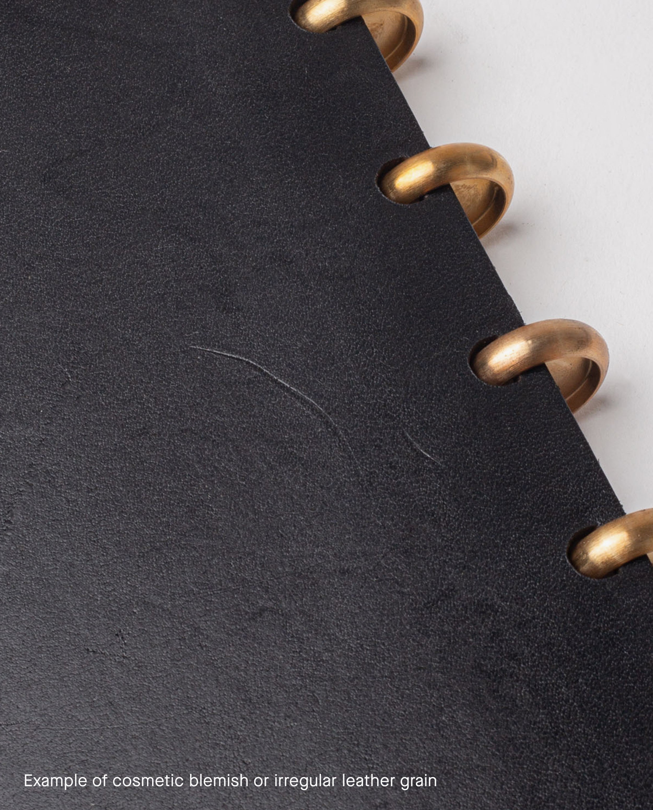 Close-up of a black full grain leather cover with brass rings and a faint scratch in the center, showing a cosmetic blemish or irregular leather grain—an ideal find for our warehouse sale on this Warehouse Item - Discbound Heirloom Journal (Black/Brass).