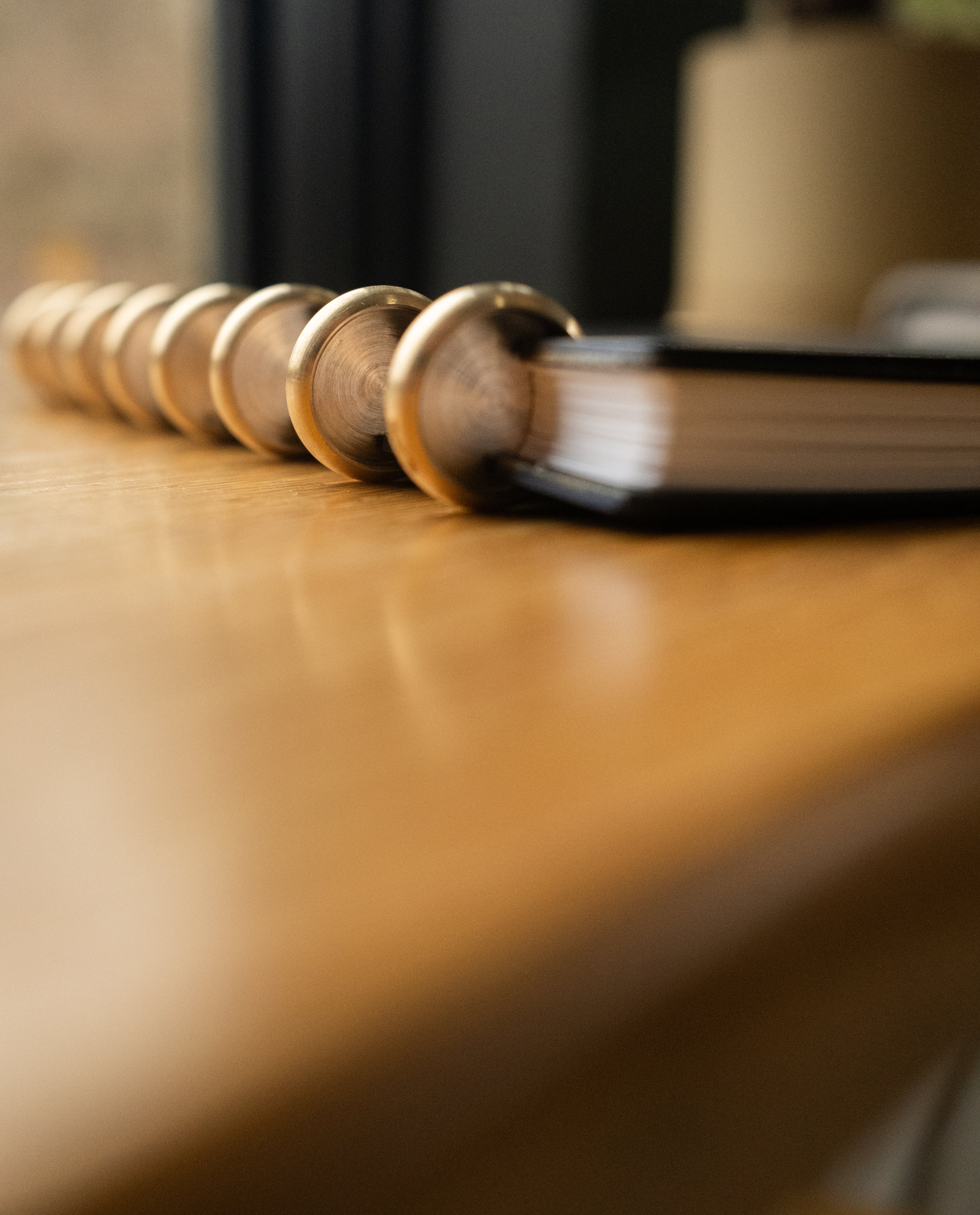 A Discbound Heirloom Journal (Black Leather - Standard 6" x 8.5") lies on a wooden surface, showcasing its durable metal rings in sharp focus against a softly blurred background.