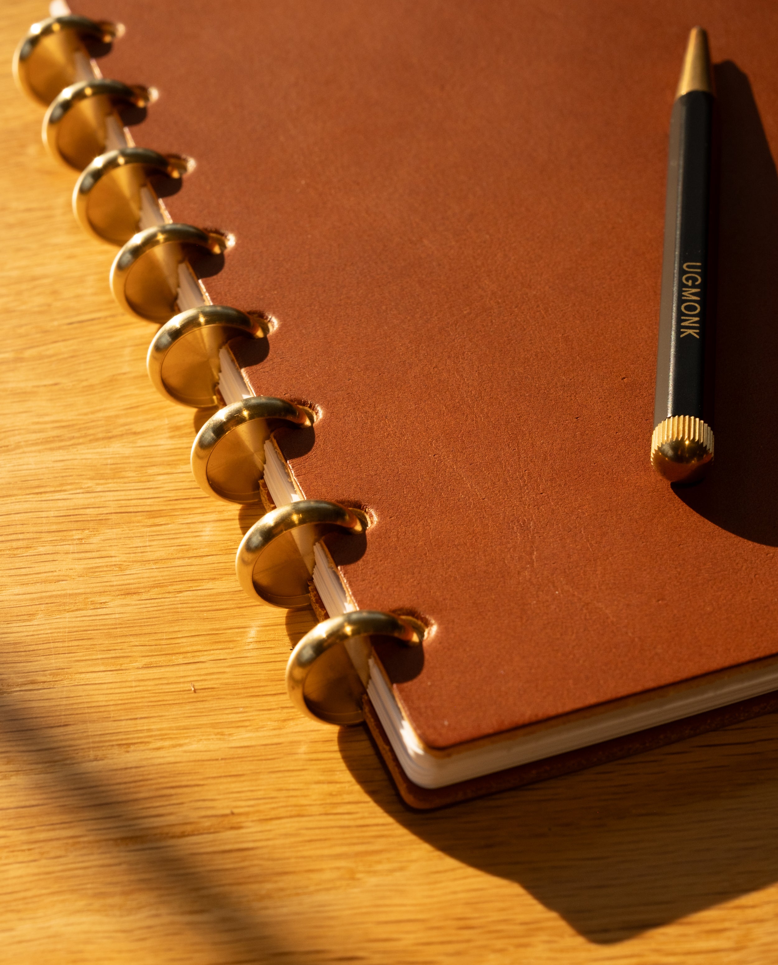 A Discbound Heirloom Journal in tan leather (standard 6" x 8.5”) with dot grid pages and a pen rests elegantly on the table.
