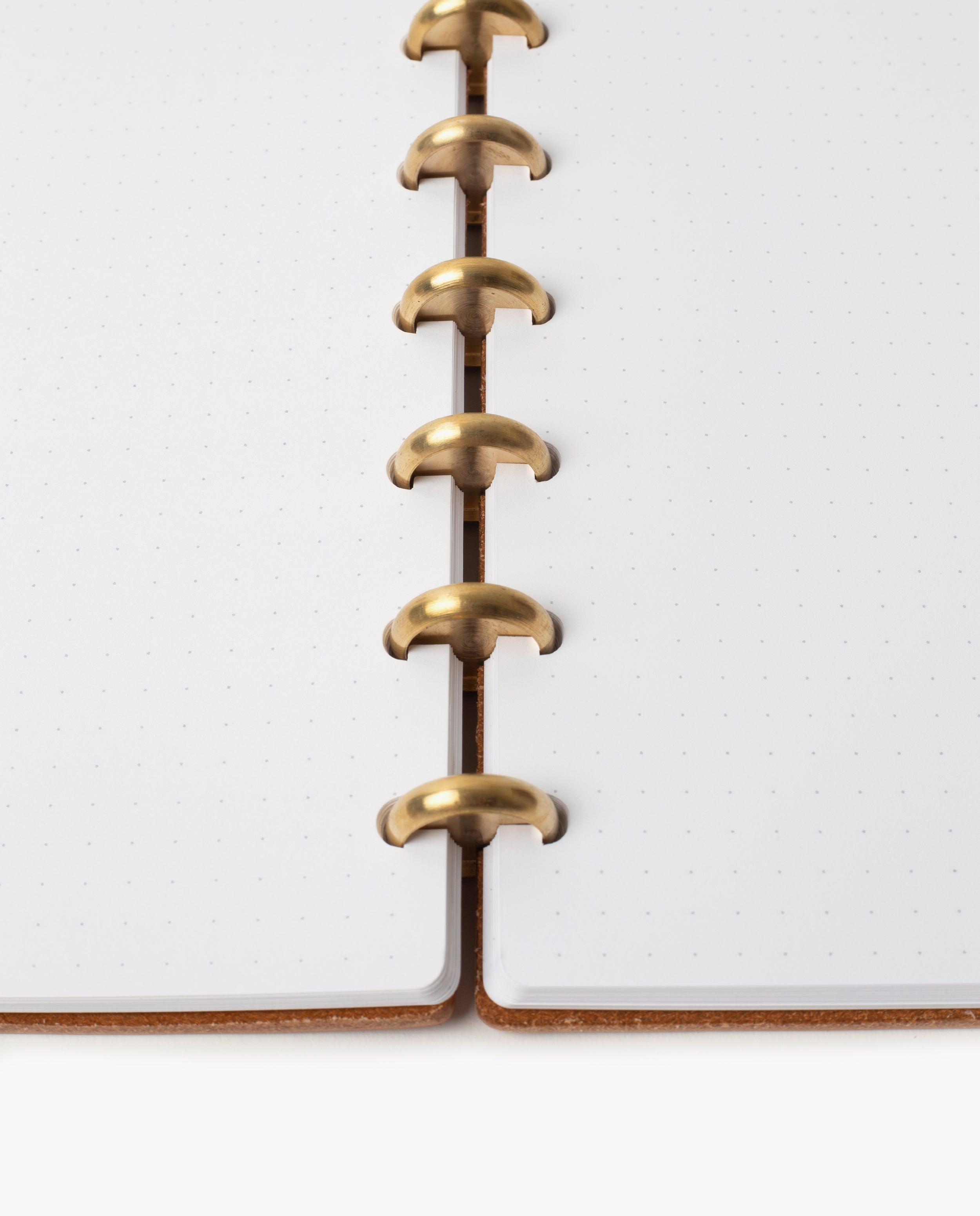 Close-up of the Discbound Heirloom Journal Bundle (Tan Leather - Standard 6" x 8.5" + 3 Refills), showing its gold-colored disc binding rings and dotted white pages. The refillable journal lies flat, highlighting the sturdy binding and pristine pages.