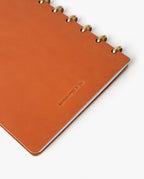 A tan full-grain leather Warehouse Item - Discbound Heirloom Journal with brass rings is shown on a white background. The cover is embossed with the words HANDCRAFTED IN USA. Only part of this refillable discbound journal is visible in the image.