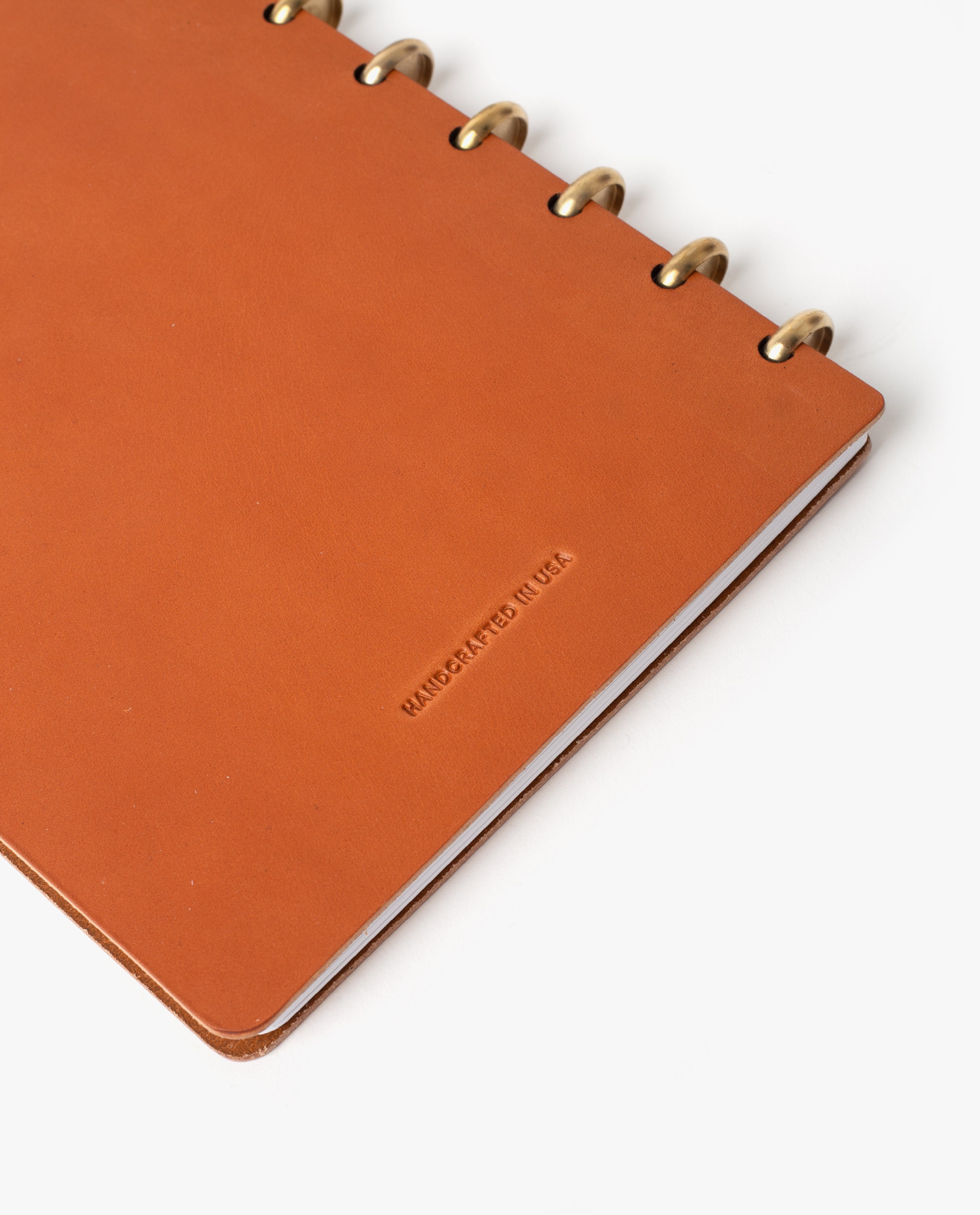 A tan full-grain leather Warehouse Item - Discbound Heirloom Journal with brass rings is shown on a white background. The cover is embossed with the words HANDCRAFTED IN USA. Only part of this refillable discbound journal is visible in the image.