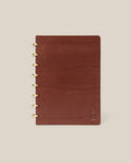 The Discbound Heirloom Journal (Brown Leather, 6" x 8.5") features refillable pages, gold disc binding, and a subtle embossed logo in the bottom right corner, shown on a plain beige background.