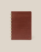 The Discbound Heirloom Journal (Brown Leather, 6" x 8.5") features refillable pages, gold disc binding, and a subtle embossed logo in the bottom right corner, shown on a plain beige background.