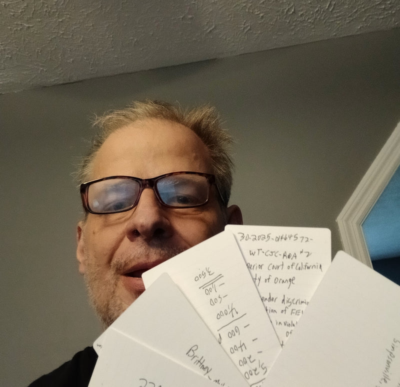 A person with glasses smiles and holds several index cards with handwritten notes, fanned out in front of their face.