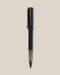 A black LAMY AL-star Rollerball pen with a transparent section near the tip is vertically centered on a plain beige background, highlighting its smooth writing experience and refillable rollerball design.