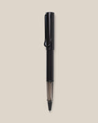 A black LAMY AL-star Rollerball pen with a transparent section near the tip is vertically centered on a plain beige background, highlighting its smooth writing experience and refillable rollerball design.