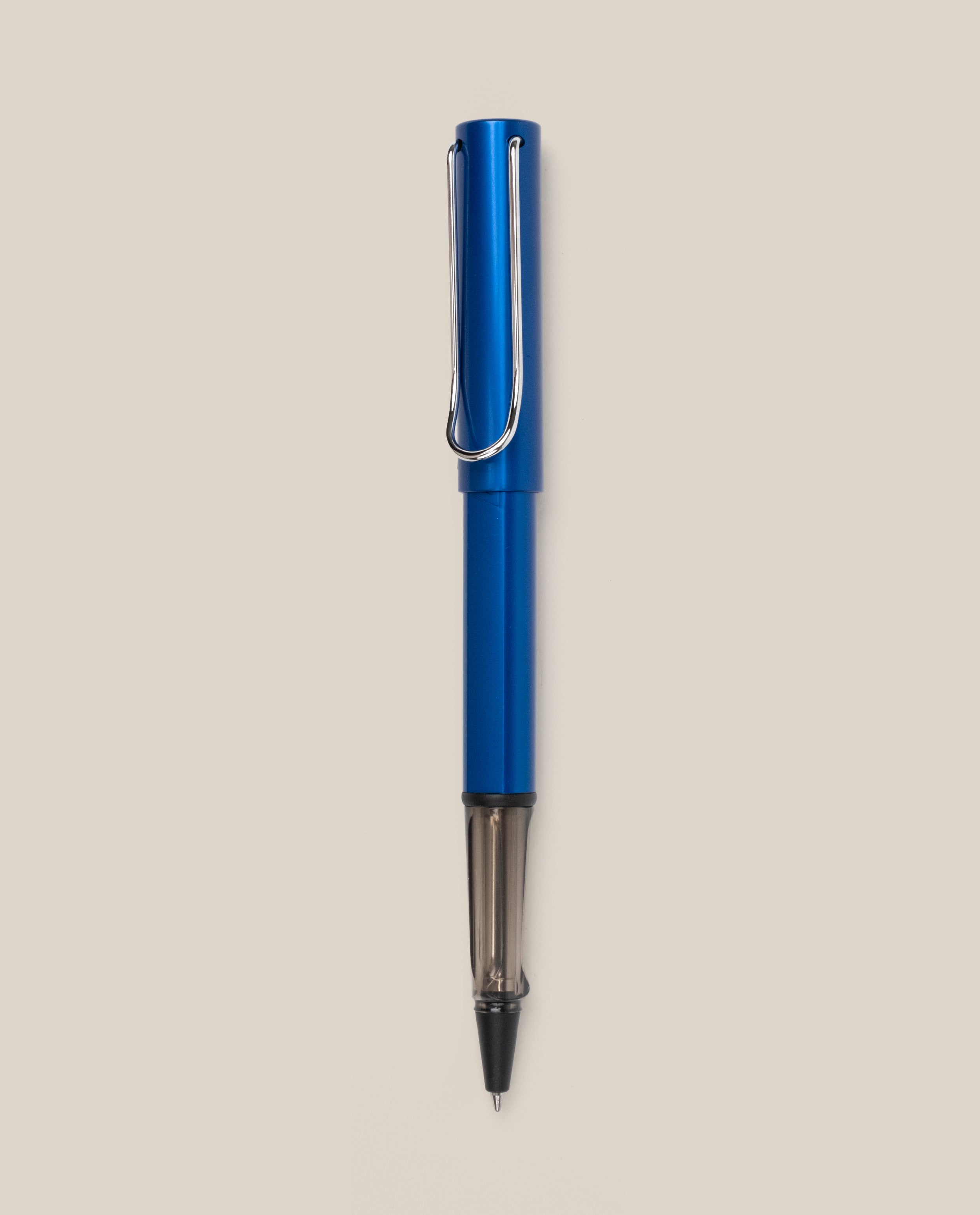 A LAMY AL-star Rollerball (Oceanblue) with a metal clip stands vertically on a light beige background, featuring smooth writing and a stylish design.