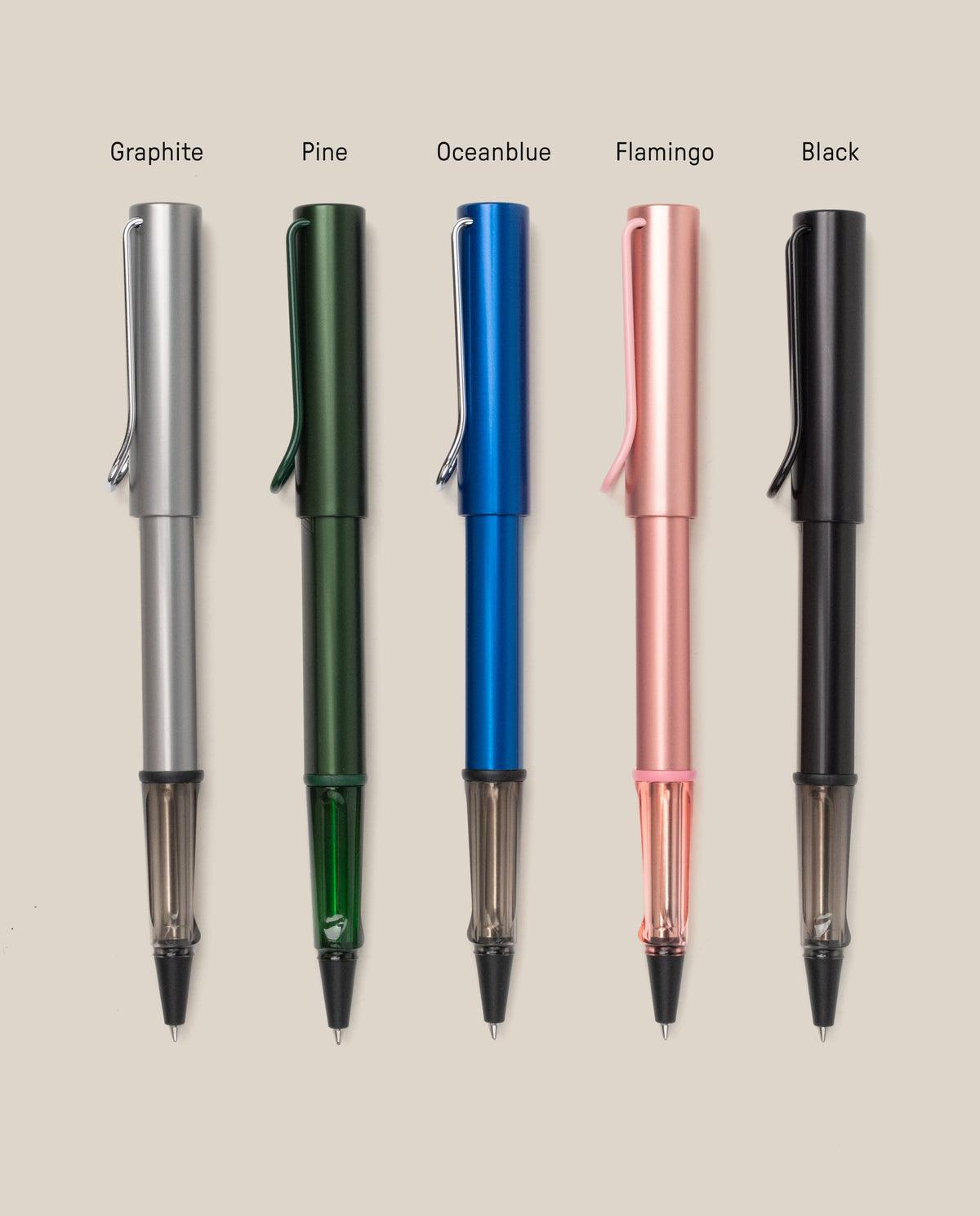 Five LAMY AL-star Rollerball pens—graphite (silver), pine (green), ocean blue, flamingo (pink), and black—are arranged vertically on a beige background. Each refillable pen is labeled above and designed for smooth writing.