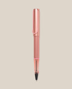 The LAMY AL-star Rollerball (Flamingo) features a pink anodized aluminum body, clear grip, and black ink tip, shown vertically on a light beige background for smooth writing.