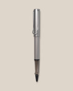 A graphite LAMY AL-star Rollerball with a sleek design stands vertically against a light beige background, highlighting its smooth writing performance and stylish, refillable rollerball pen construction.