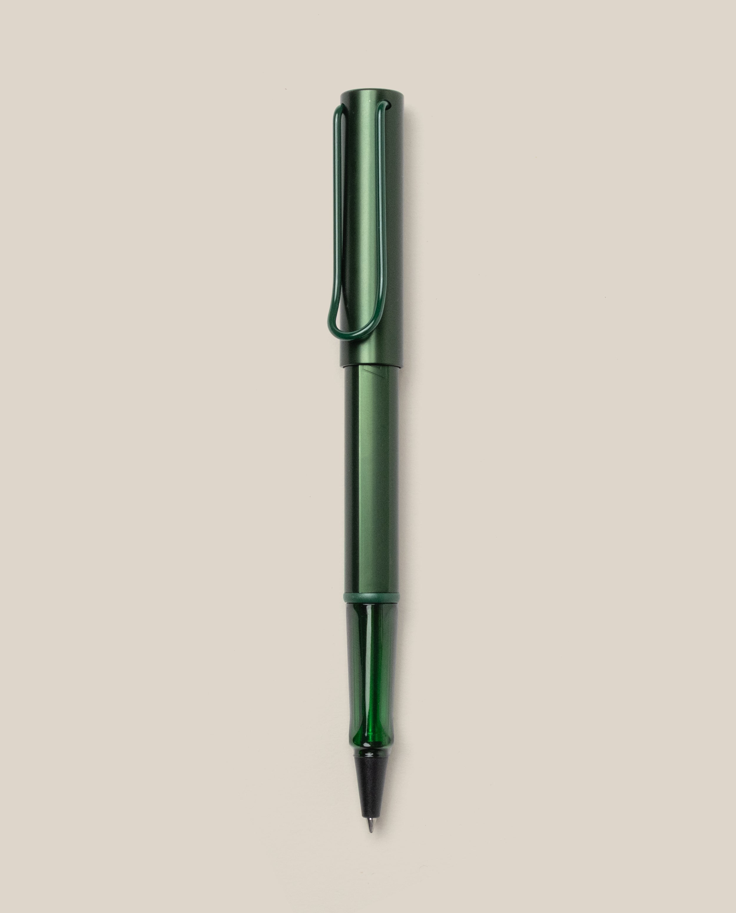A LAMY AL-star Rollerball (Pine) pen in green metallic, with matching cap and clip, is displayed vertically on a plain light beige background. This refillable pen ensures smooth, effortless writing.
