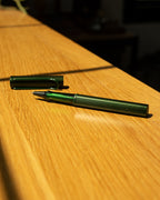 A LAMY AL-star Rollerball (Pine) with its cap off rests on a sunlit wooden surface, casting a soft shadow—ready to deliver smooth writing whenever inspiration strikes.