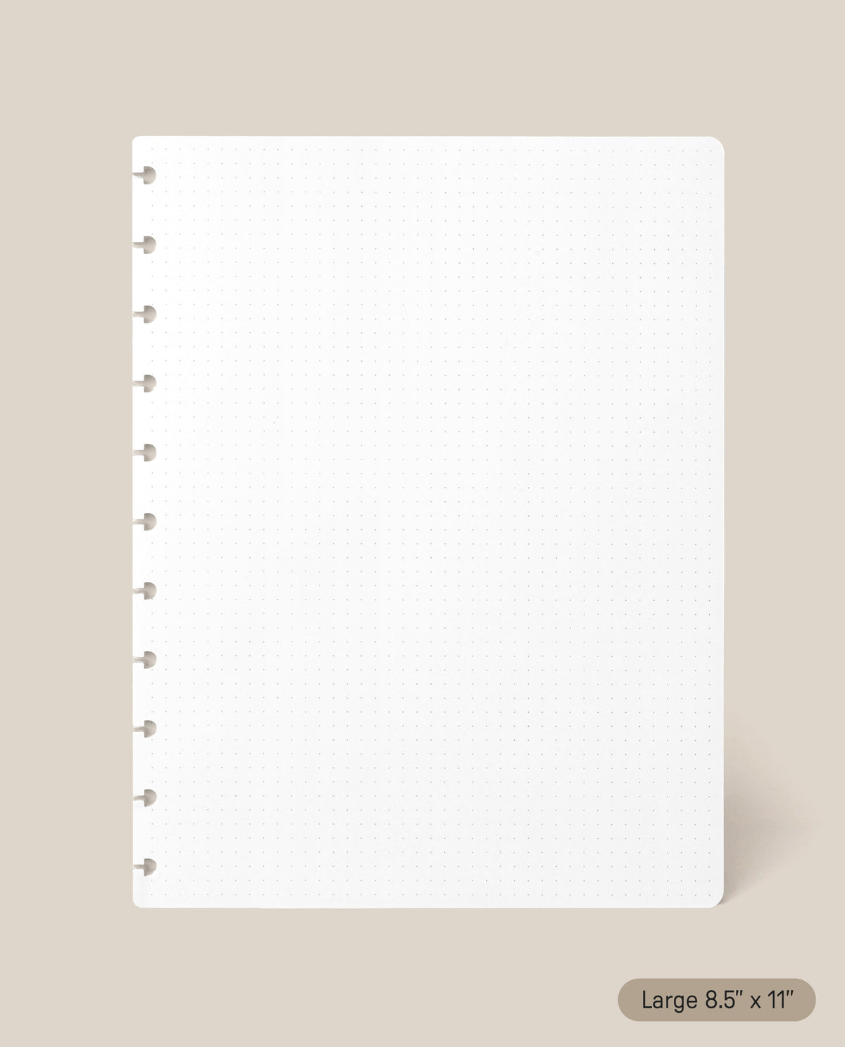 A Large Discbound Journal Refill - Dot Grid (8.5″ x 11″) page in crisp white, featuring round disc-binding holes along the left side and a subtle label in the corner that reads “Large 8.5″ x 11″,” is displayed on a beige background—ideal for refilling your discbound journal.