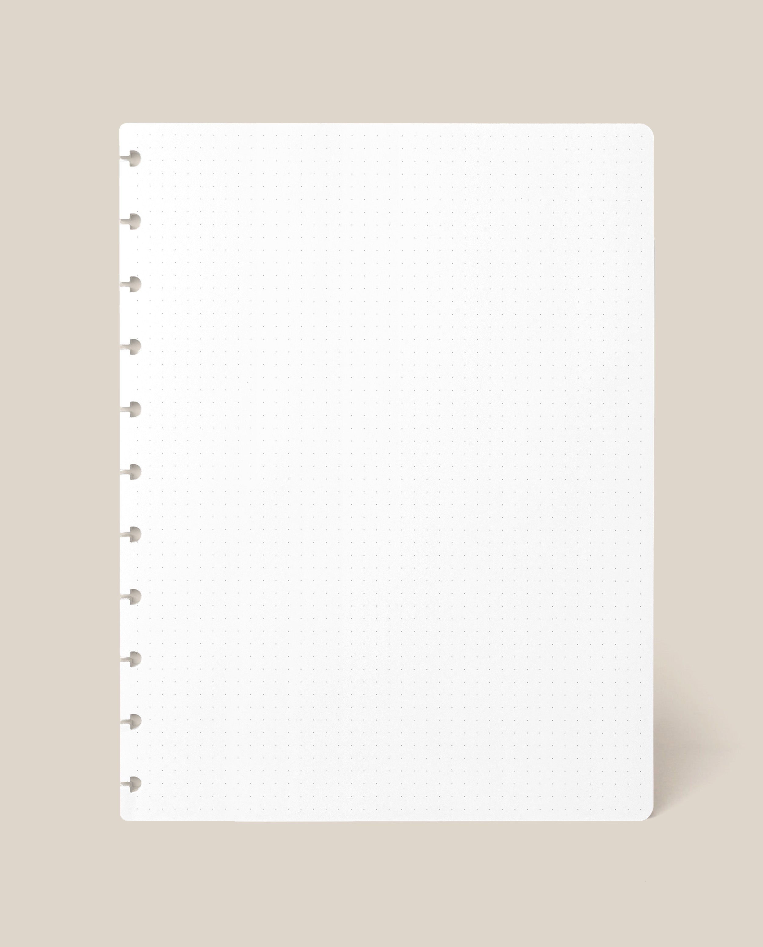 A Large Discbound Journal Refill - Dot Grid (8.5″ x 11″) sheet, featuring a square white page with round discbound holes along the left edge, is displayed against a light beige background.