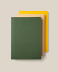 A set of three Layflat Notebook Bundle (Set of 3) notebooks are stacked on a beige background, featuring a dark green notebook with an embossed geometric pattern on top, a tan notebook in the middle, and a yellow notebook on the bottom. Each has rounded corners and durable Smyth sewn bindings that allow for effortless writing across every page.