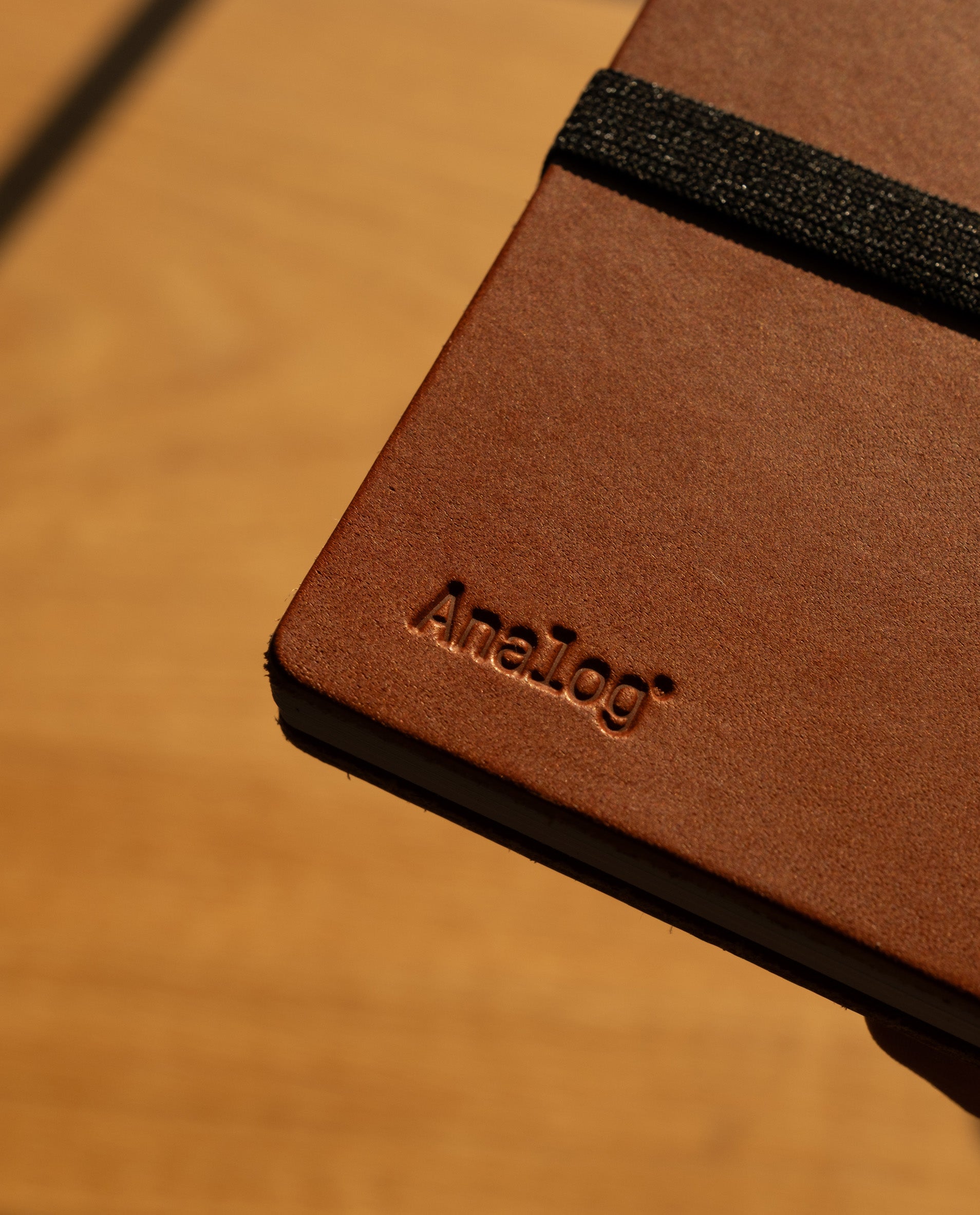 A close-up of the Leather Discbound Analog + 3 Refills (Tan) notebook, showcasing its full-grain tan leather covers with "Analog" embossed on the cover and secured by a black elastic band.