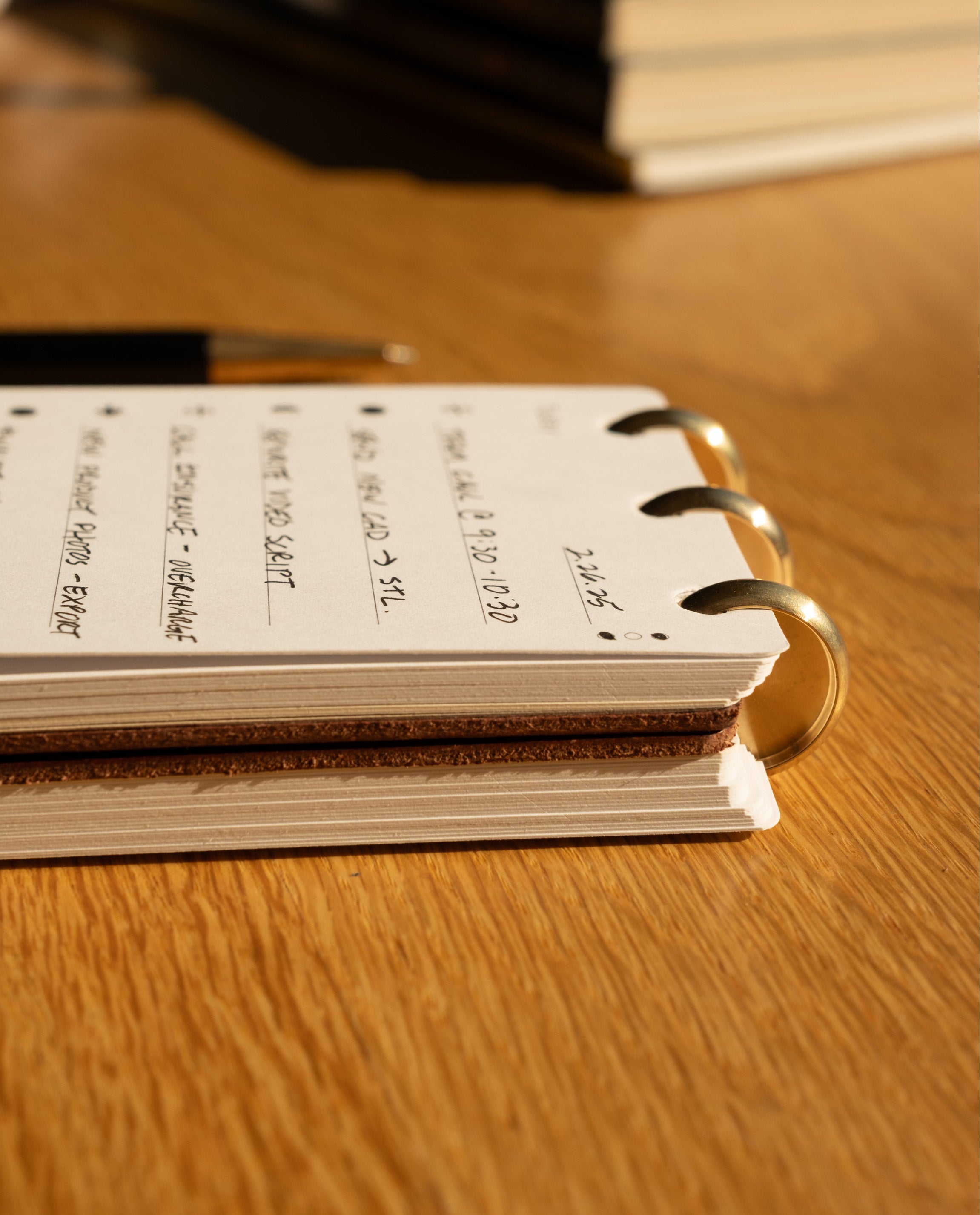 A close-up of the Leather Discbound Analog + 3 Refills (Tan) featuring handwritten notes and a pen resting on top, all arranged on a wooden surface.