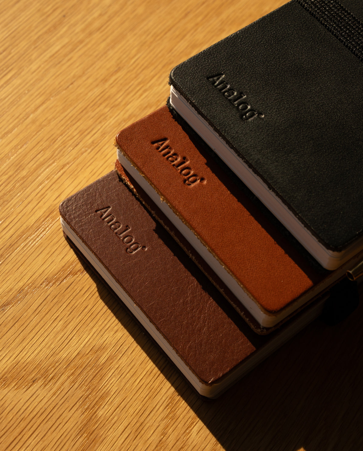 A Leather Discbound Analog + 3 Refills (Tan) notebook with a full-grain leather cover rests on a wooden surface, sunlight casting soft shadows across the scene.