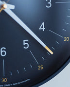 Close-up of the Lemnos Essent Wall Clock (Navy) displaying the time at approximately 4:25. This elegant designer clock features bold white numbers, gold-tipped hands, and fine minute markers with small yellow numerals at intervals—an aesthetic that would be perfectly at home among iF Design Award winners.