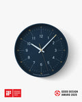 The Lemnos Essent Wall Clock (Navy), featuring a sleek modern design with crisp white numerals and elegant gold hands, is displayed. Highlighting its status as a true designer wall clock, the iF DESIGN AWARD 2025 and GOOD DESIGN AWARD 2025 logos are shown in the bottom left corner.