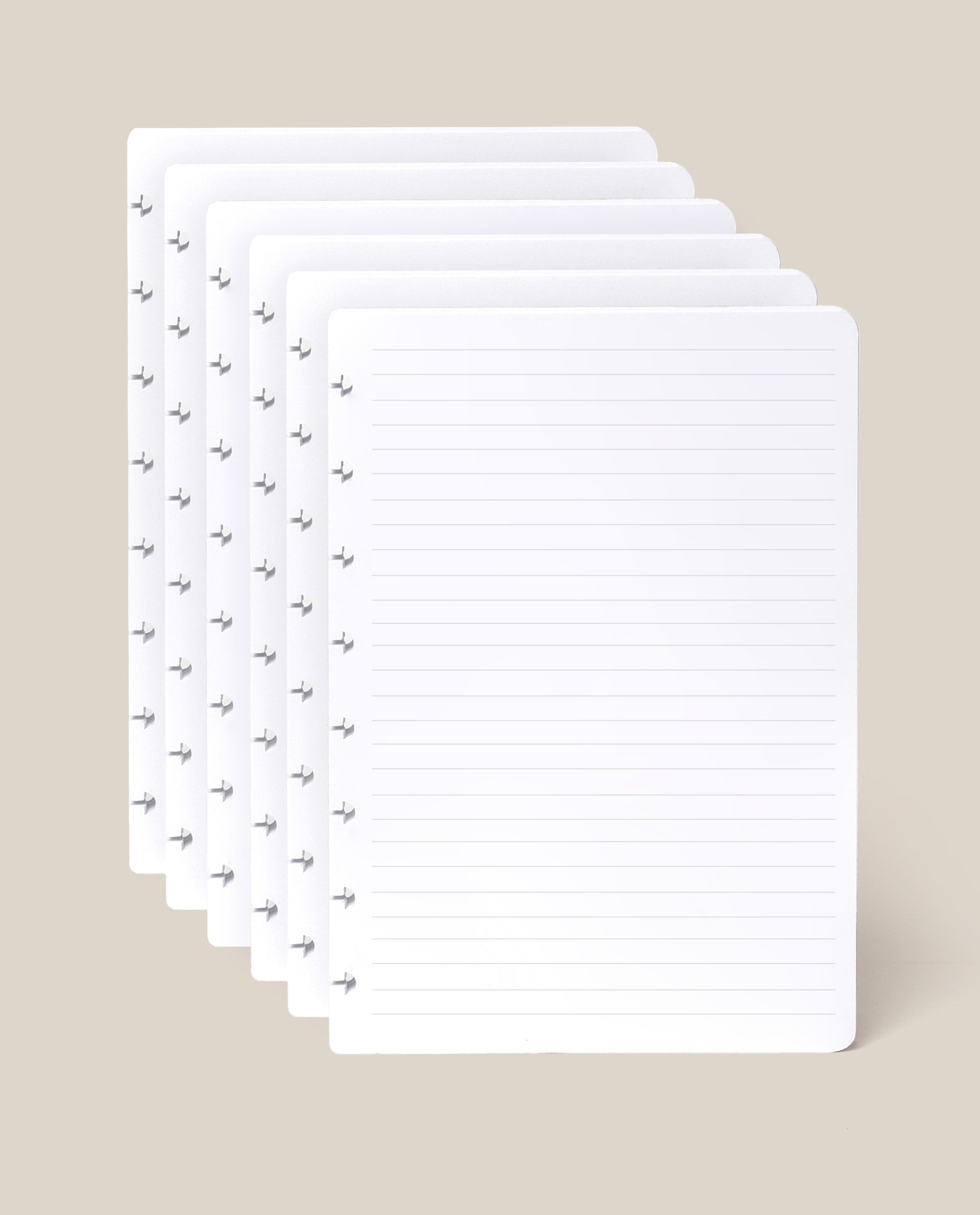 Six sheets of the Discbound Journal Refill - Lined (Standard 6″ x 8.5″), each with neatly lined pages and discbound punched holes along the left edge, are stacked against a light beige background—perfect for adding to your Heirloom Discbound Journal.
