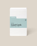 A stack of Analog Lined Cards - Small, in white 3x5 with a blue-green label, 50 cards made from 100lb uncoated cardstock, displayed upright on a beige background.