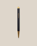 A Ugmonk Pen (Leuchtturm1917 Drehgriffel - Black) with gold accents and UGMONK in gold lettering on the barrel, shown against a plain beige background.