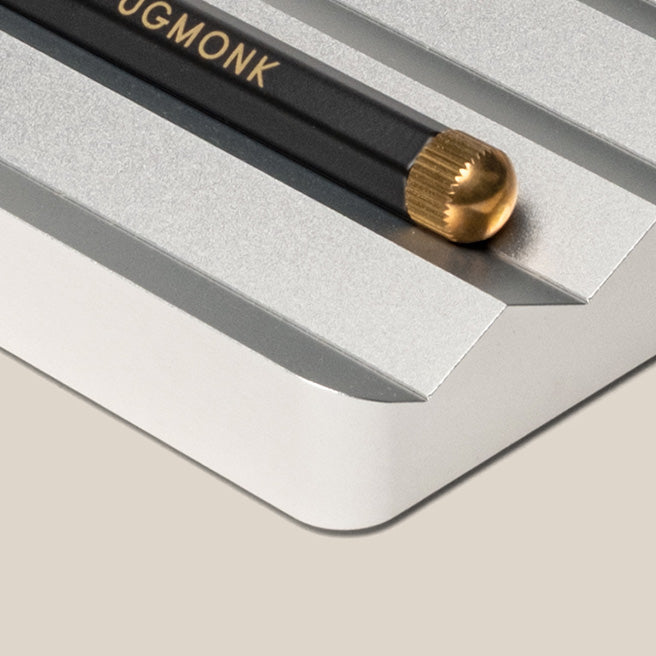 A black pencil with a gold eraser end rests in a groove on a metallic, silver desk organizer with angled edges.