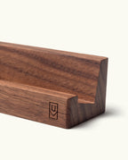 A close-up of the Analog Weekly Card Holder (Walnut), a handcrafted geometric stand with a small stylized U and V logo on its side, made in Pennsylvania.