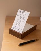An Analog Dot Grid Card from the Small (3-Pack) sits upright in a wooden holder on a light desk, featuring handwritten notes for ad creative and video production—ideal for organized note taking. A black and gold pen rests nearby.