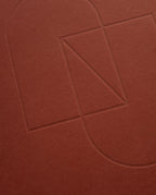 Embossed geometric shapes—a rectangle, triangle, and two semicircles—are outlined on the textured cover of the maroon Layflat Notebook.