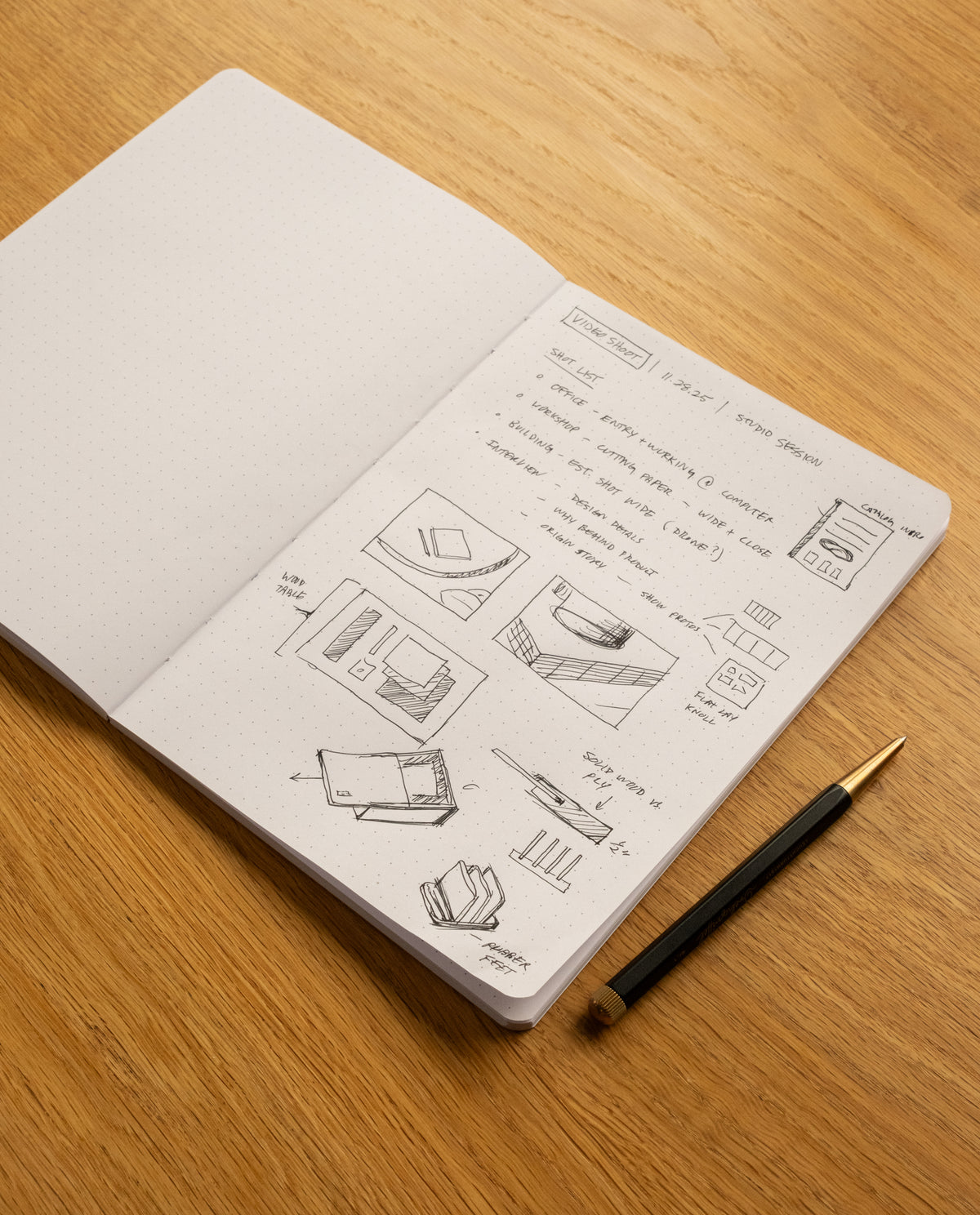 An open Layflat Notebook (Yellow) with dot grid pages displays sketches and notes for a design project, featuring diagrams of a box and user interface. A black and gold pen rests on the wooden desk beside the notebook.