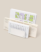 Three open notebooks stand upright. The back features colorful floor plans; the middle, handwritten notes and a meal plan. In front, a small calendar peeks from its cover next to the Analog Card Organizer (Silver Aluminum) for sleek card storage.