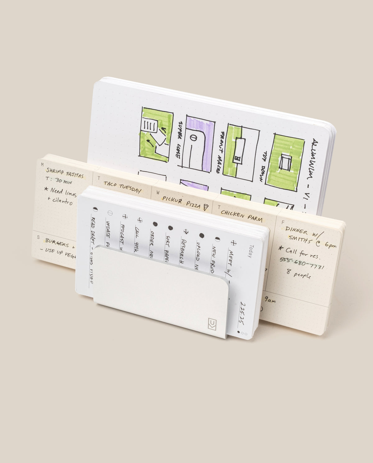 Three open notebooks stand upright. The back features colorful floor plans; the middle, handwritten notes and a meal plan. In front, a small calendar peeks from its cover next to the Analog Card Organizer (Silver Aluminum) for sleek card storage.