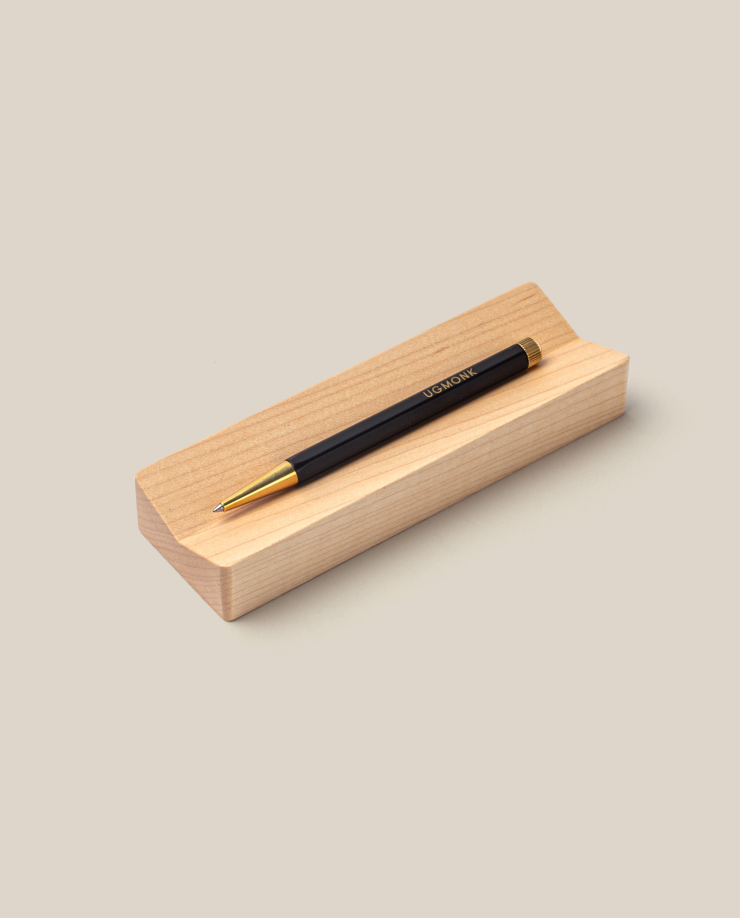A stylish black and gold gel ink pen from The Pen & Pen Tray Bundle (Black/Maple) rests on a light maple pen tray against a beige background.