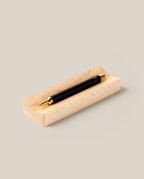A black and gold pen rests on the Pen Tray (Maple), creating an elegant desk accessory against a plain beige background.