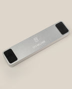 The Analog Pen Tray (Silver Aluminum) is a solid aluminum rectangular pen tray with UGMONK branding and logo on top, two black rectangular pads on each end, displayed on a light beige background—a sleek desk accessory.