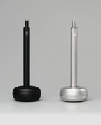 Two HMM Paperweight Pen Stands (Black), with hexagonal handles and round bases, are displayed side by side on a plain gray background, offering a quirky desk accessory that doubles as a pen stand or paperweight.
